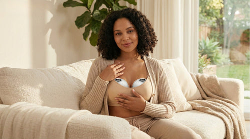 Woman sitting on a couch wearing a beige cardigan with a mamaroo breastfit breast pump on her chest.