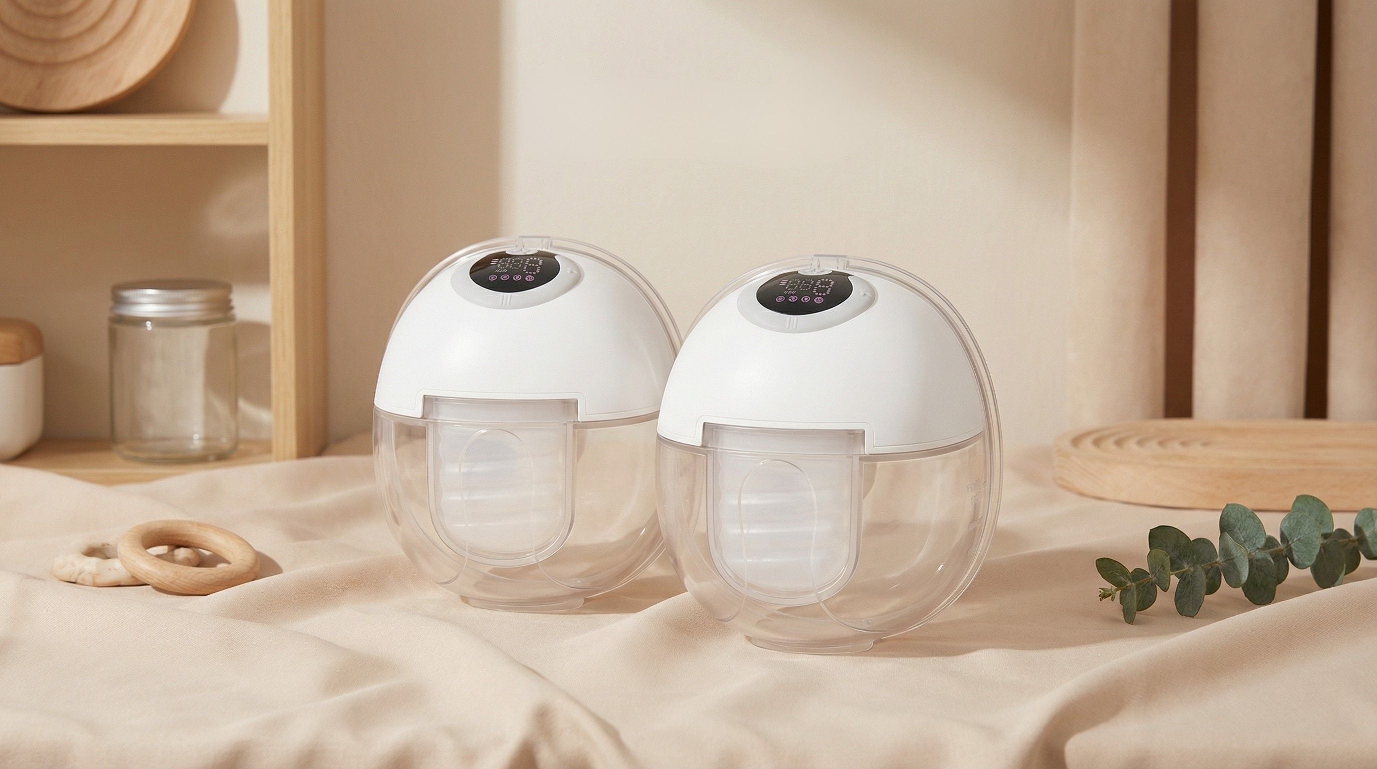 Two white and clear spherical breast pumps on a neutral background with wooden shelves and greenery.