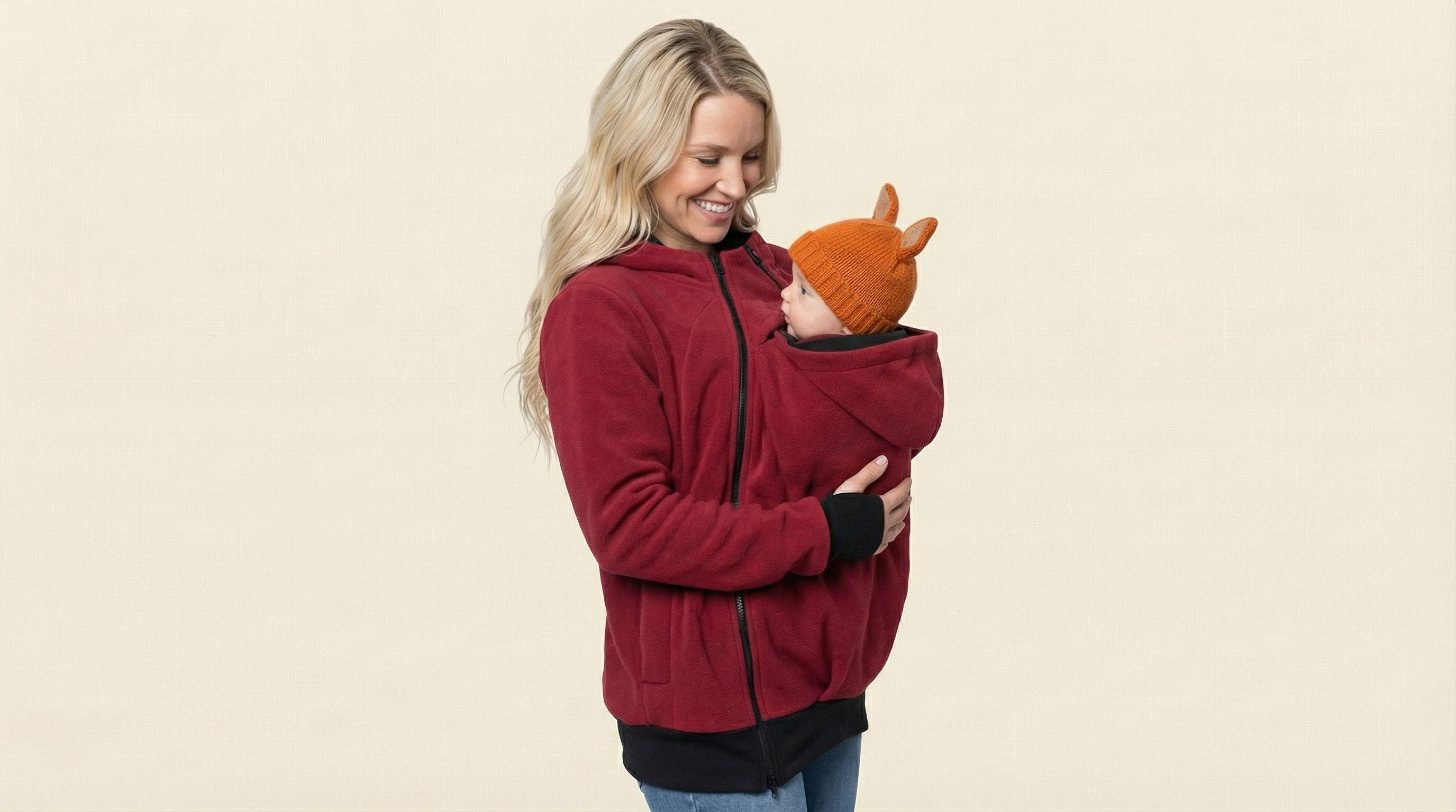 Woman wearing a red jacket holding a baby against a beige background