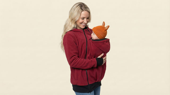 Woman wearing a red jacket holding a baby against a beige background